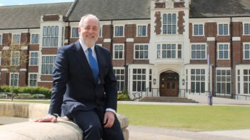 Image of Professor Nick Jennings sitting outside loughborough university by a fountain wearing a blue suit with a light blue tie.
